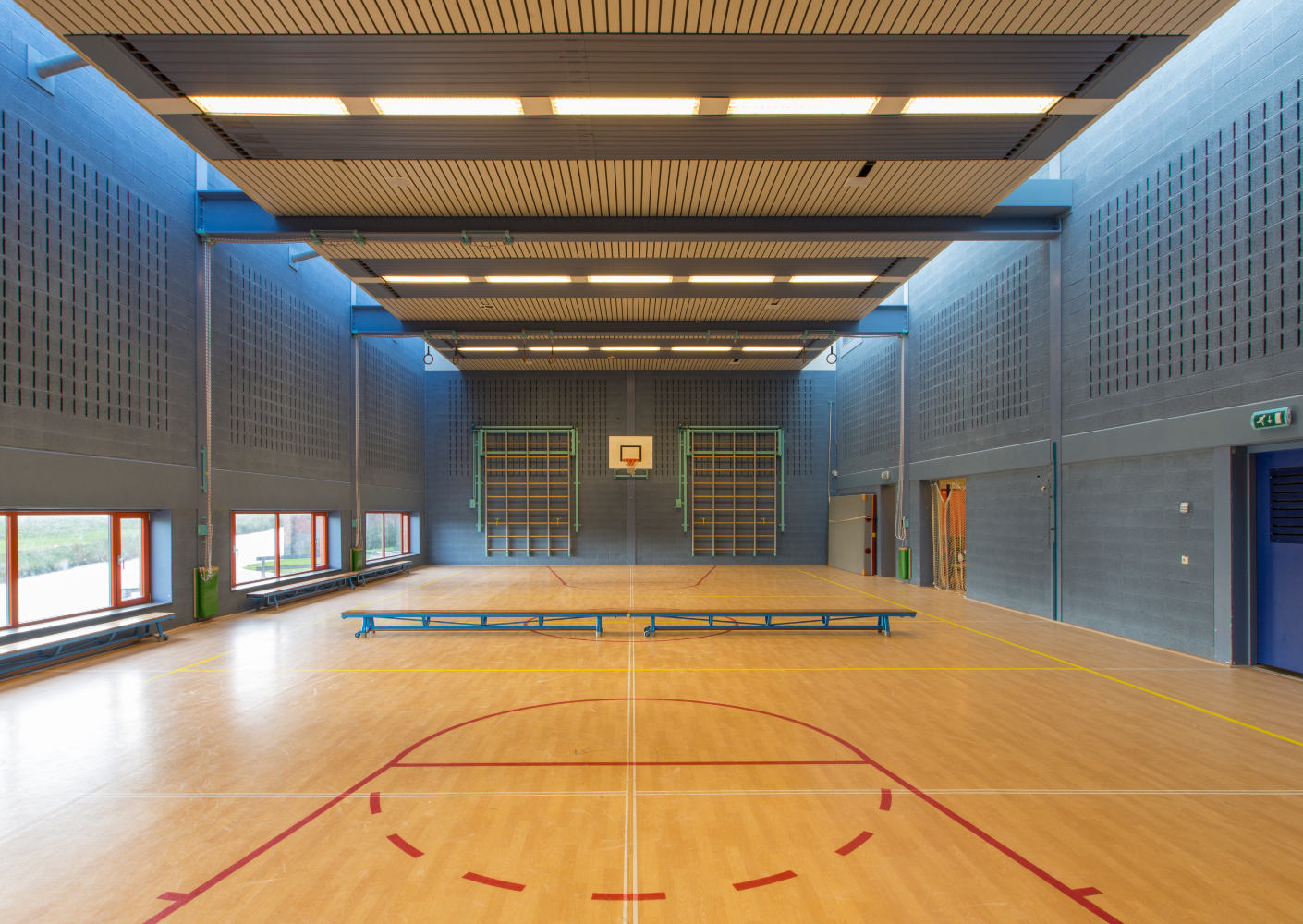 Wandafwerking; niet alleen decoratief maar ook functioneel! Gymzaal met blauwe muren en banken in het midden