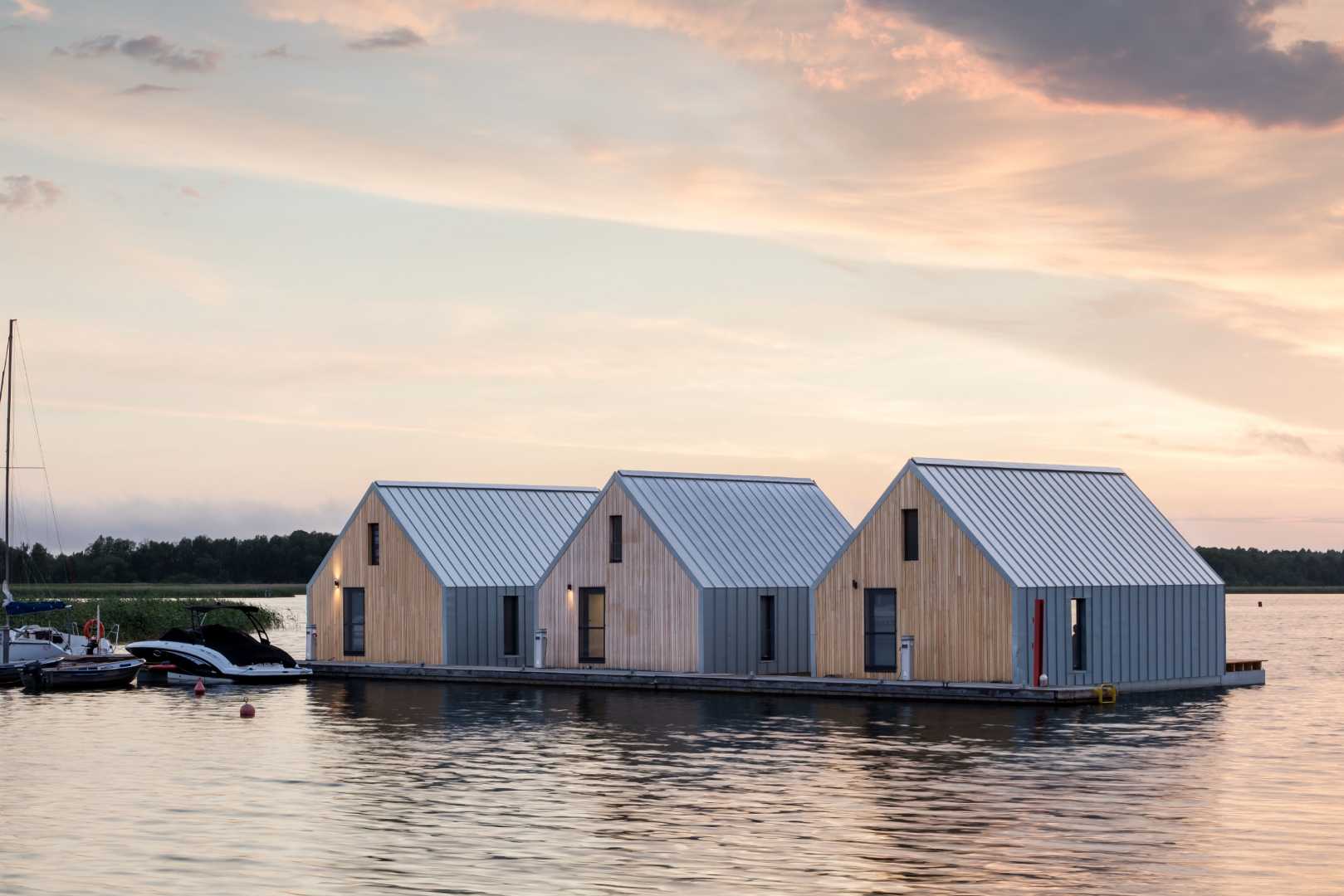 Drie drijvende vakantiewoningen op een meer in Polen. De daken en gevels die bekleed zijn met een RHEINZINK prePATINA ECO ZINC blue-grey, schitteren zachtjes in de ondergaande zon.