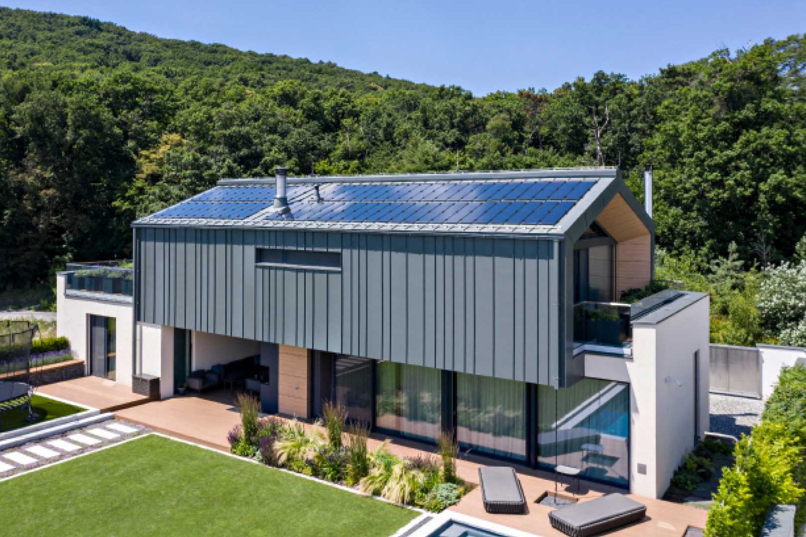 Prachtige moderne villa met zwembad dat in een groen heuvelachtig landschap staat, het dak en de gevels zijn bekleed met RHEINZINK prePATINA ECO ZINC op het dak liggen RHEINZINK-PV zonnepanelen.